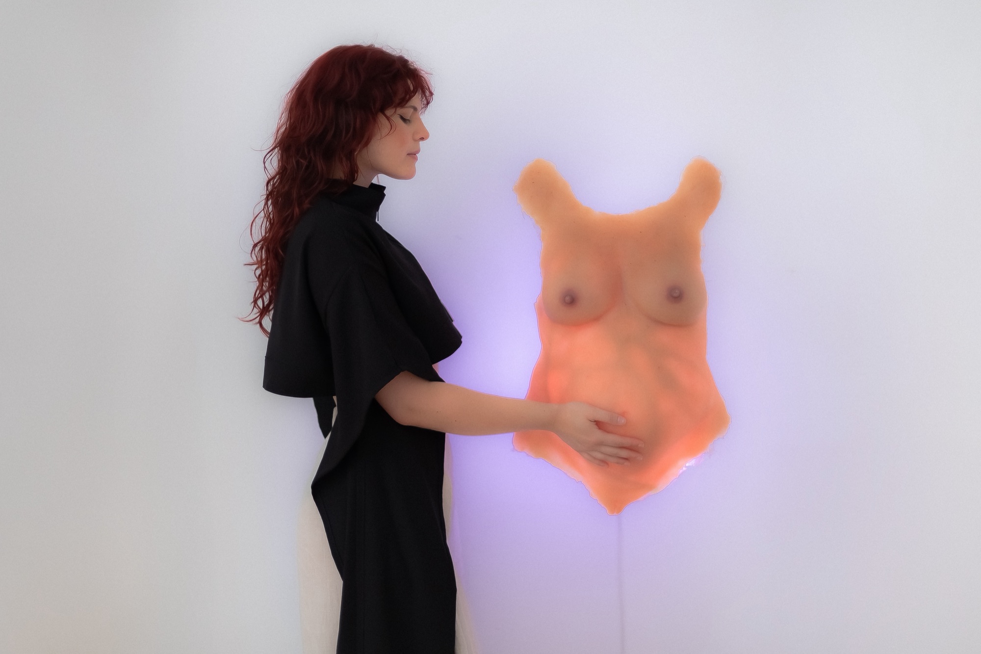 Manuela in profile with her hand on the glowing torso